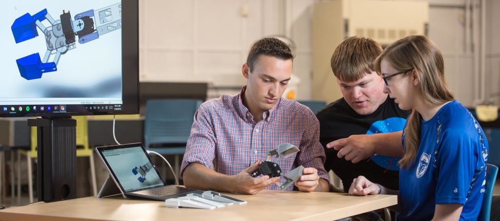 Engineering Students looking at a robotic arm